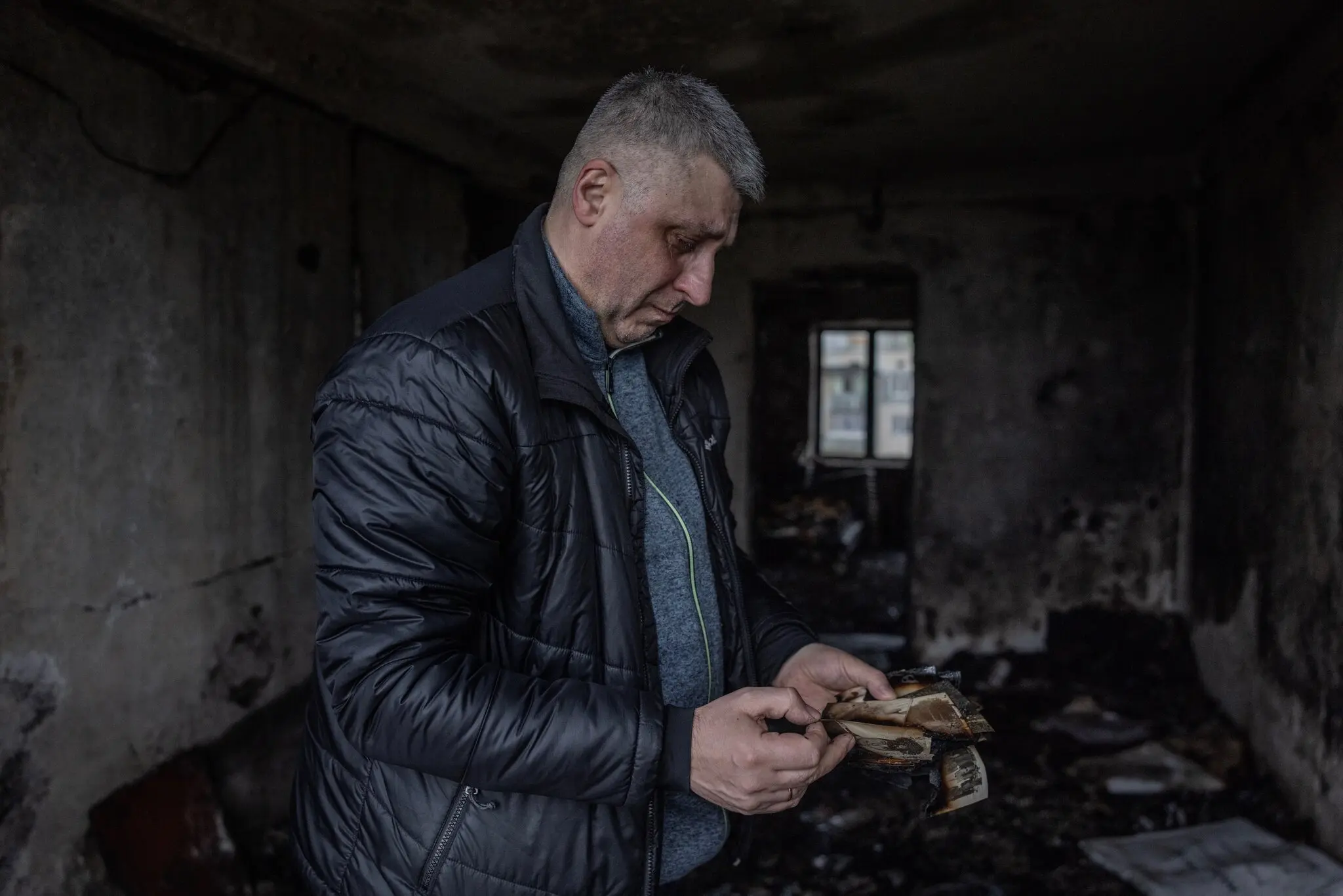 Микола Заруцький розглядає обвуглені сімейні фотографії у квартирі, де він виріс і де його мати загинула від російського безпілотника.